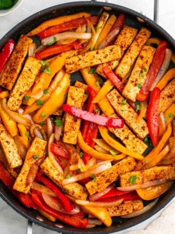 Tofu fajitas with peppers and onions topped with fresh cilantro in a skillet
