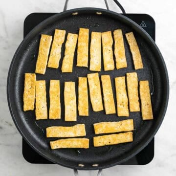Tofu cooking in a skillet until golden