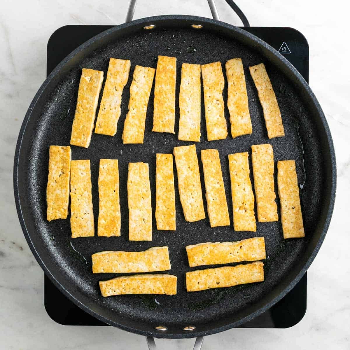 Tofu cooking in a skillet until golden
