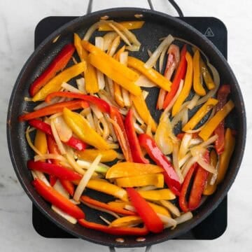 Onion and bell peppers cooking in a skillet
