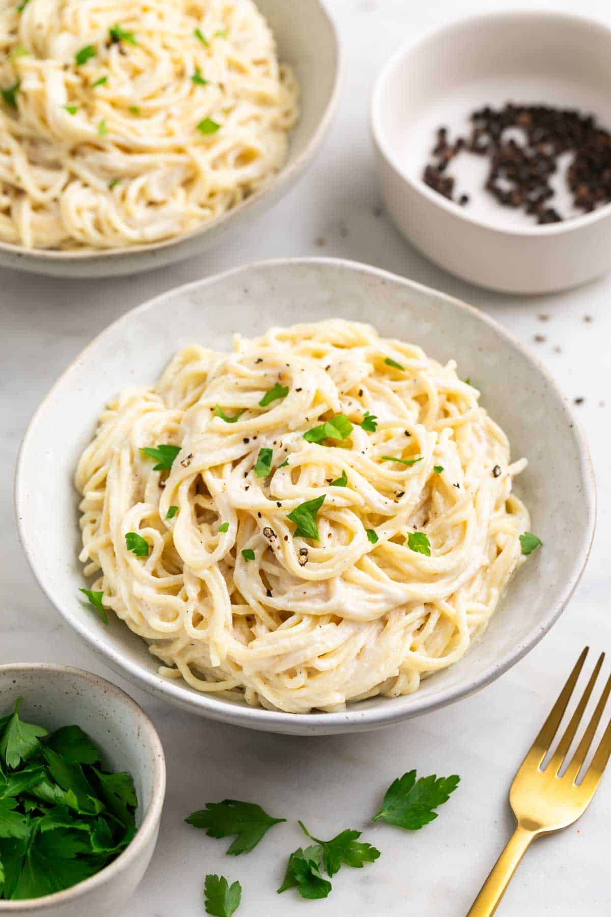 Two plates of silken tofu pasta sauce with spaghetti garnished with parsley and black pepper