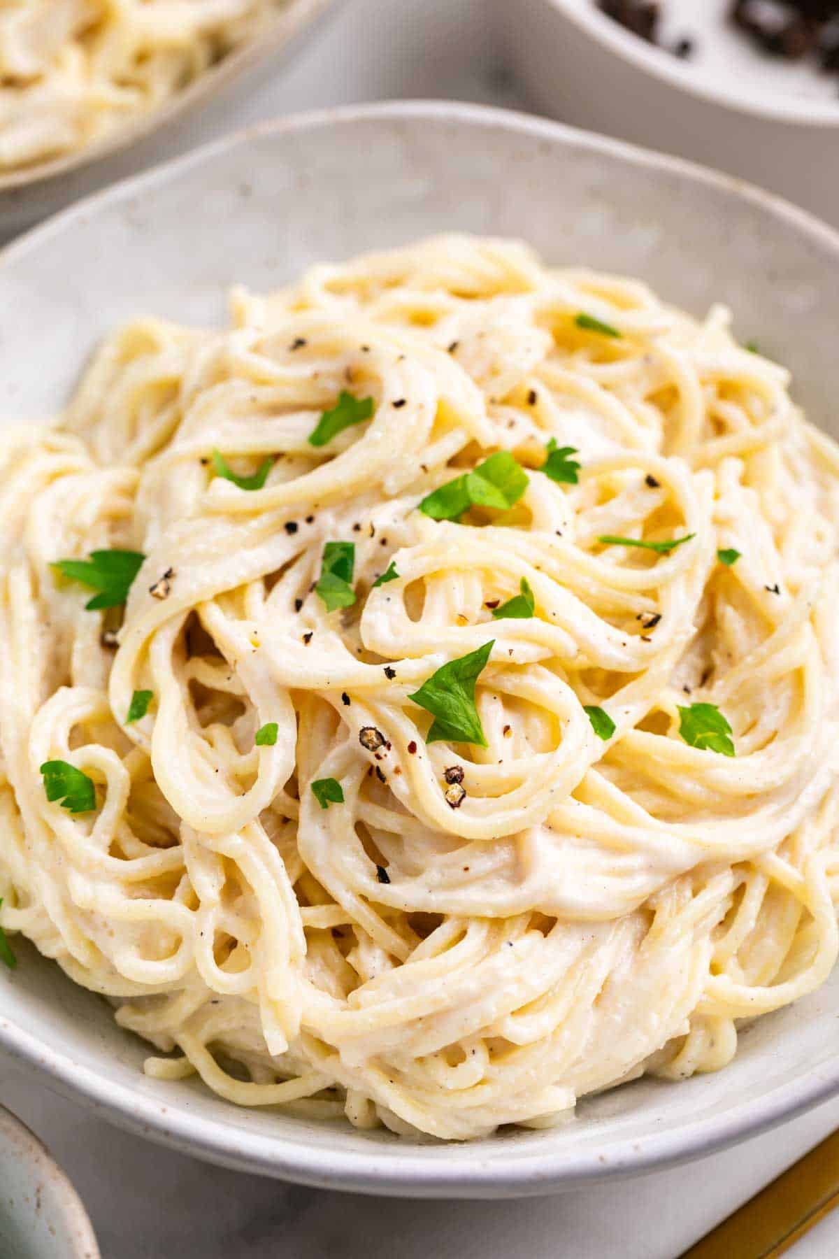Two bowls of creamy tofu pasta with spaghetti, garnished with parsley and black pepper