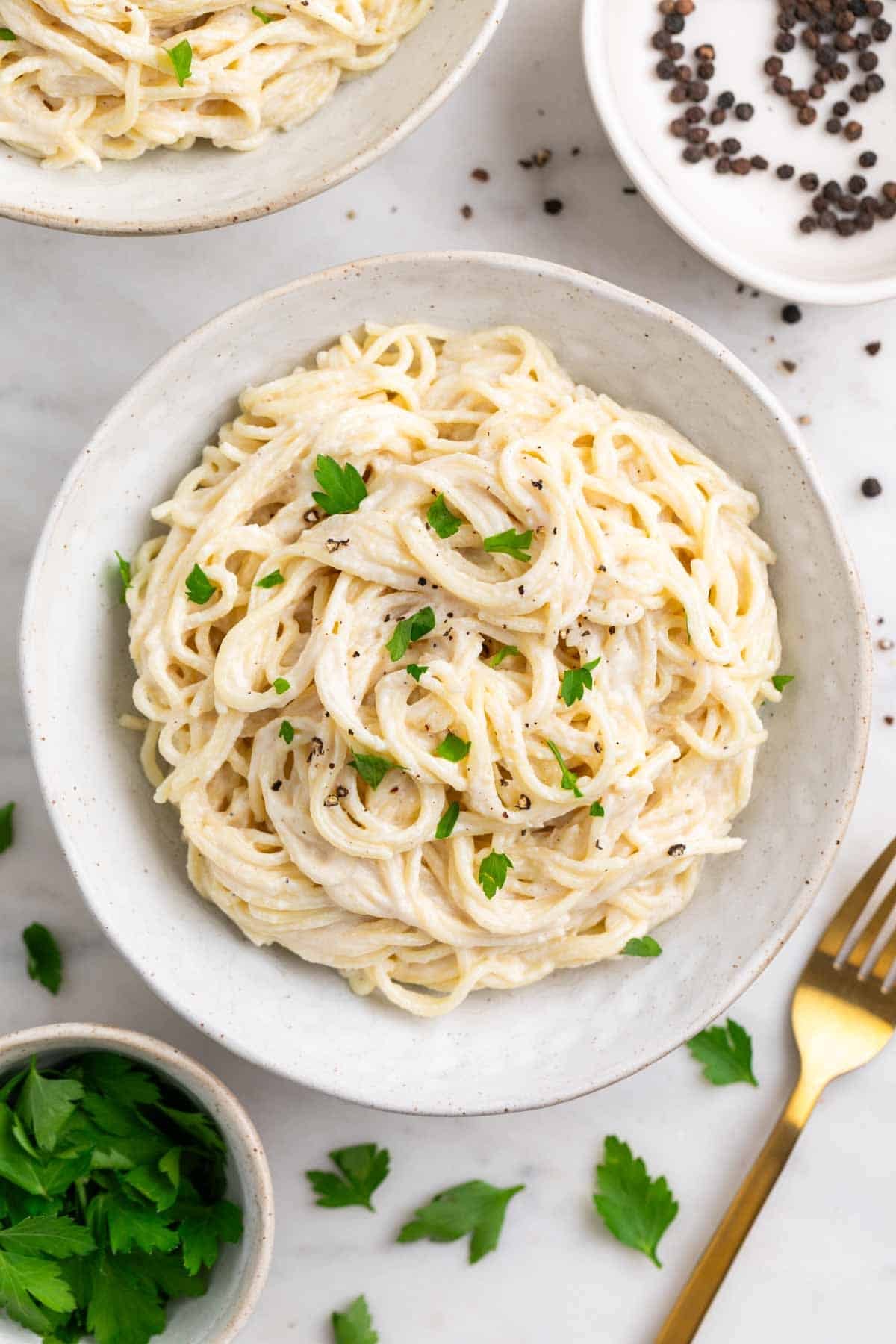 Spaghetti with tofu pasta sauce on two plates, finished with parsley and black pepper