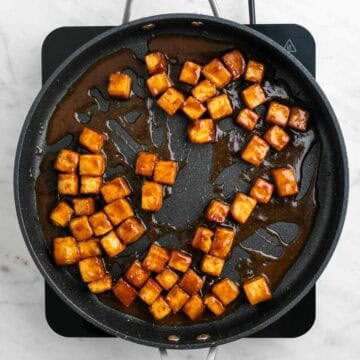 Crispy tofu cooking in a pan with sauce