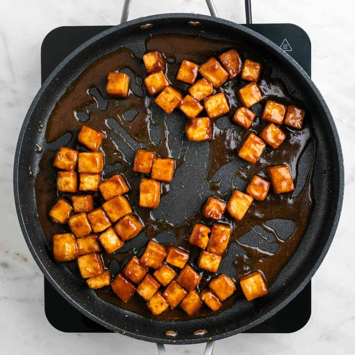Crispy tofu cooking in a pan with sauce