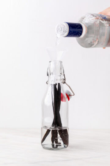 Pouring vodka into a glass bottle with vanilla beans inside