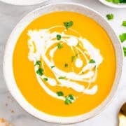 Vegan carrot soup in two bowls topped with coconut milk and parsley, with bread on the side