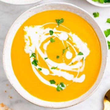 Vegan carrot soup in two bowls topped with coconut milk and parsley, with bread on the side