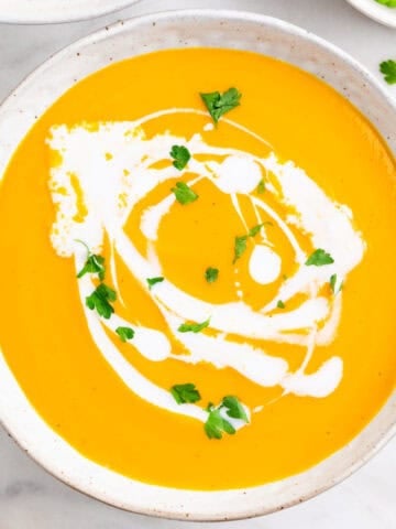 Vegan carrot soup in two bowls topped with coconut milk and parsley, with bread on the side