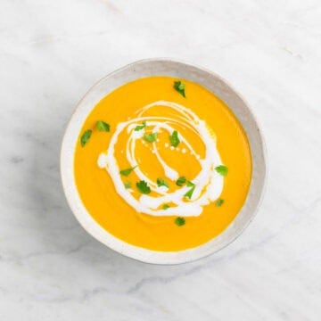 Vegan carrot soup served in a bowl with coconut milk and parsley