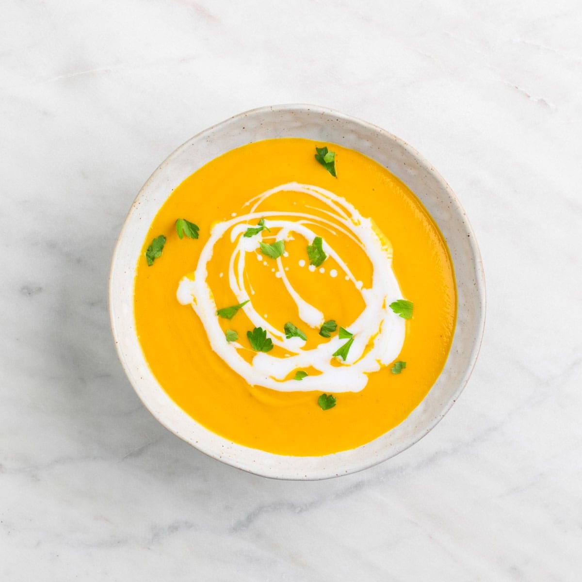 Vegan carrot soup served in a bowl with coconut milk and parsley