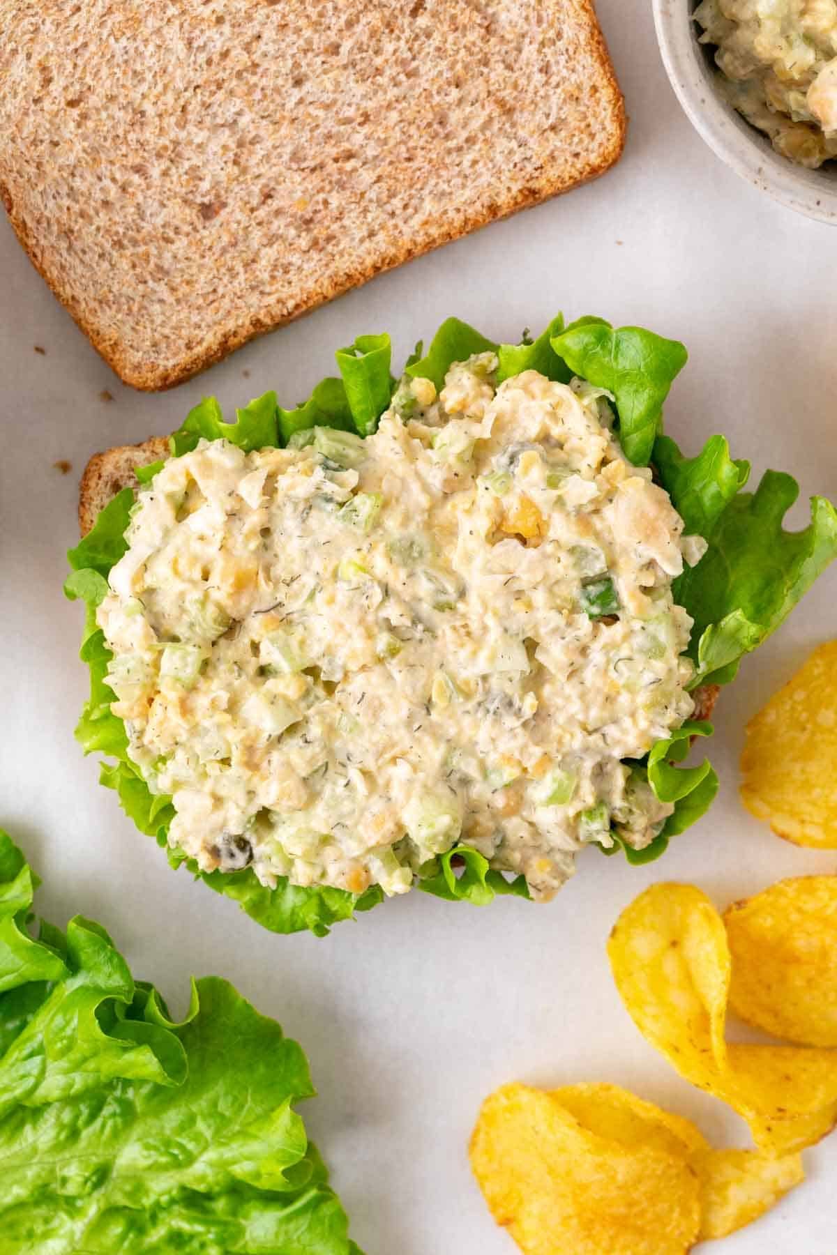Vegan chickpea salad sandwich open-faced with lettuce and served with potato chips