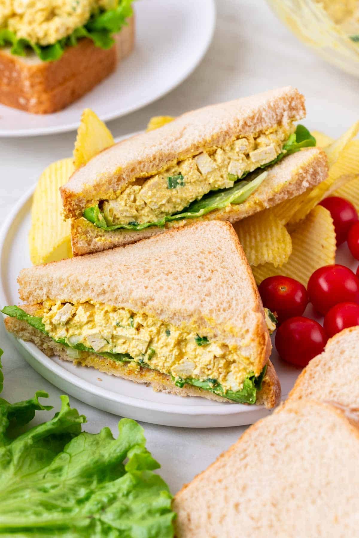 Plate with two tofu egg salad sandwiches, cherries, and chips