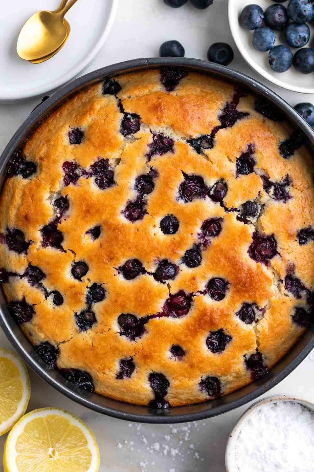Vegan lemon blueberry cake in a pan with fresh blueberries and a halved lemon