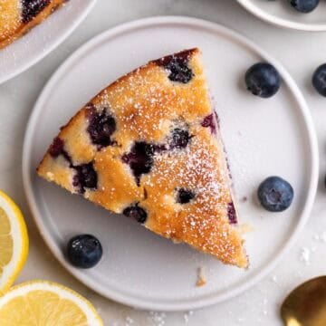Slice of vegan lemon blueberry cake dusted with powdered sugar on a plate