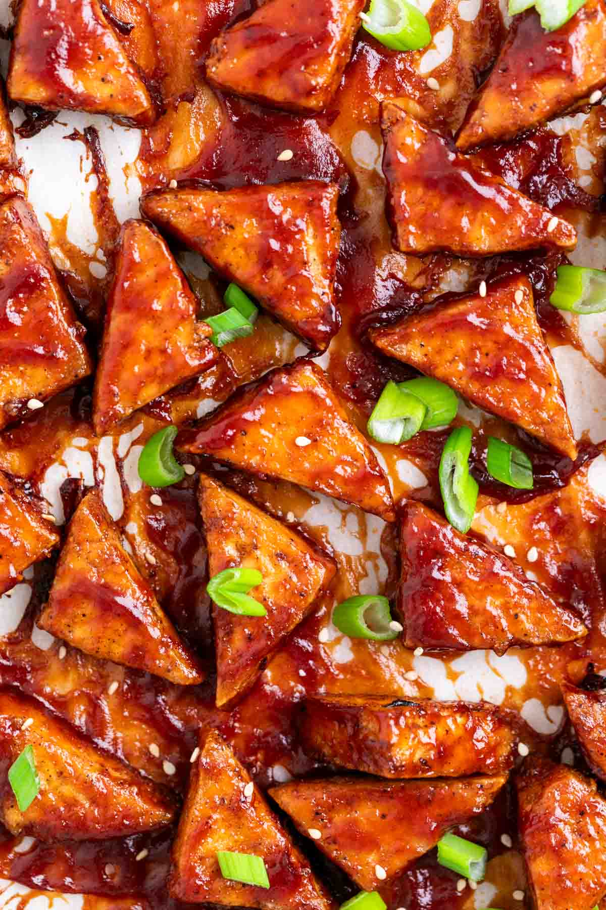 BBQ tofu triangles topped with green onions and sesame seeds on a white background