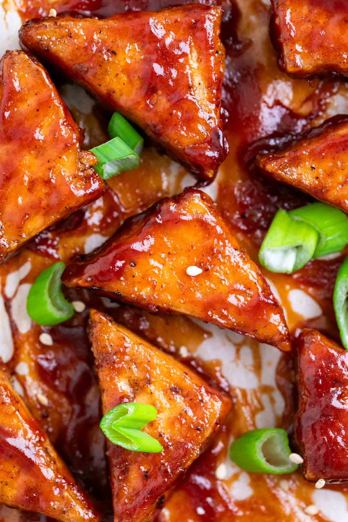 Baked BBQ tofu triangles garnished with green onions and sesame seeds