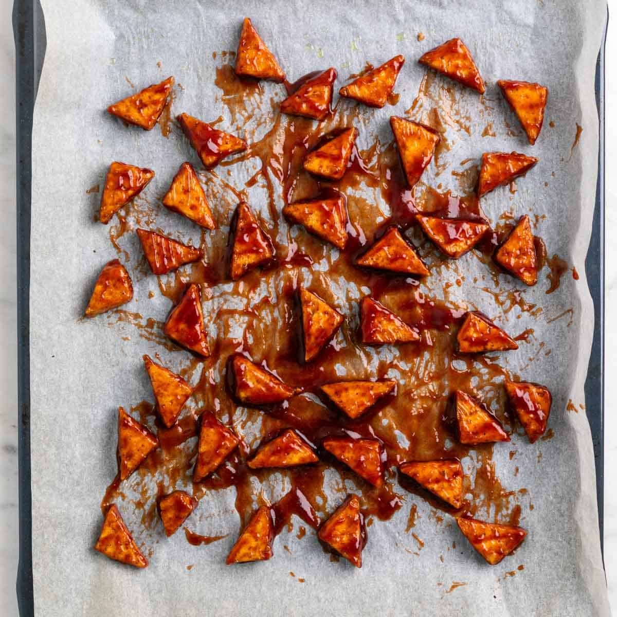 Baked tofu triangles coated with BBQ sauce before baking