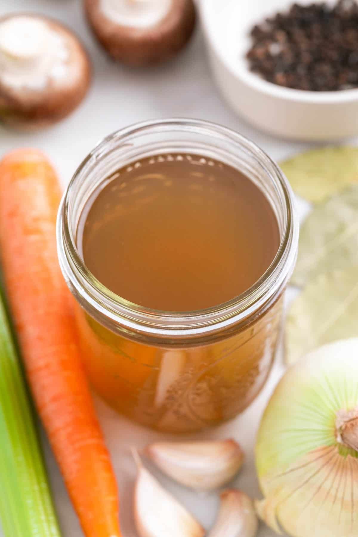 Glass jar with homemade vegetable broth and ingredients around it