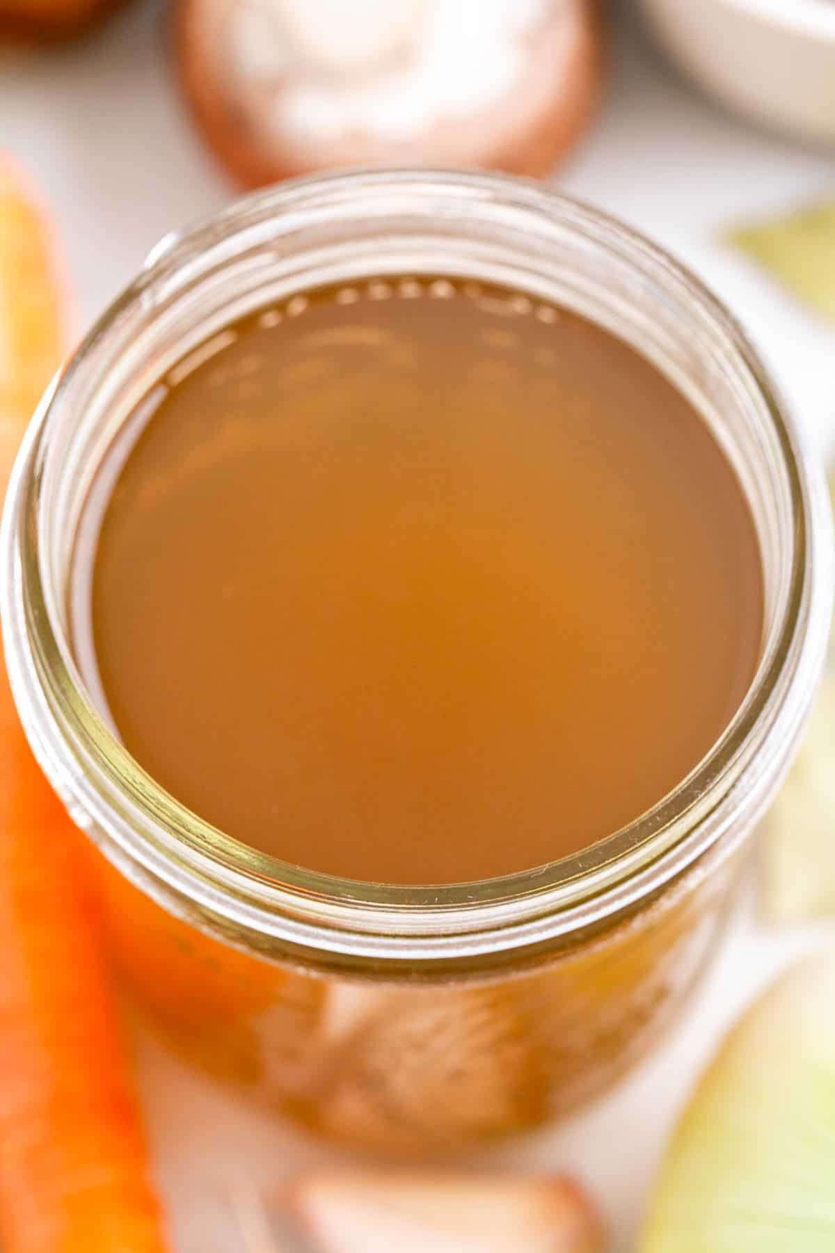 Homemade vegetable broth in a jar with vegetables and herbs around it