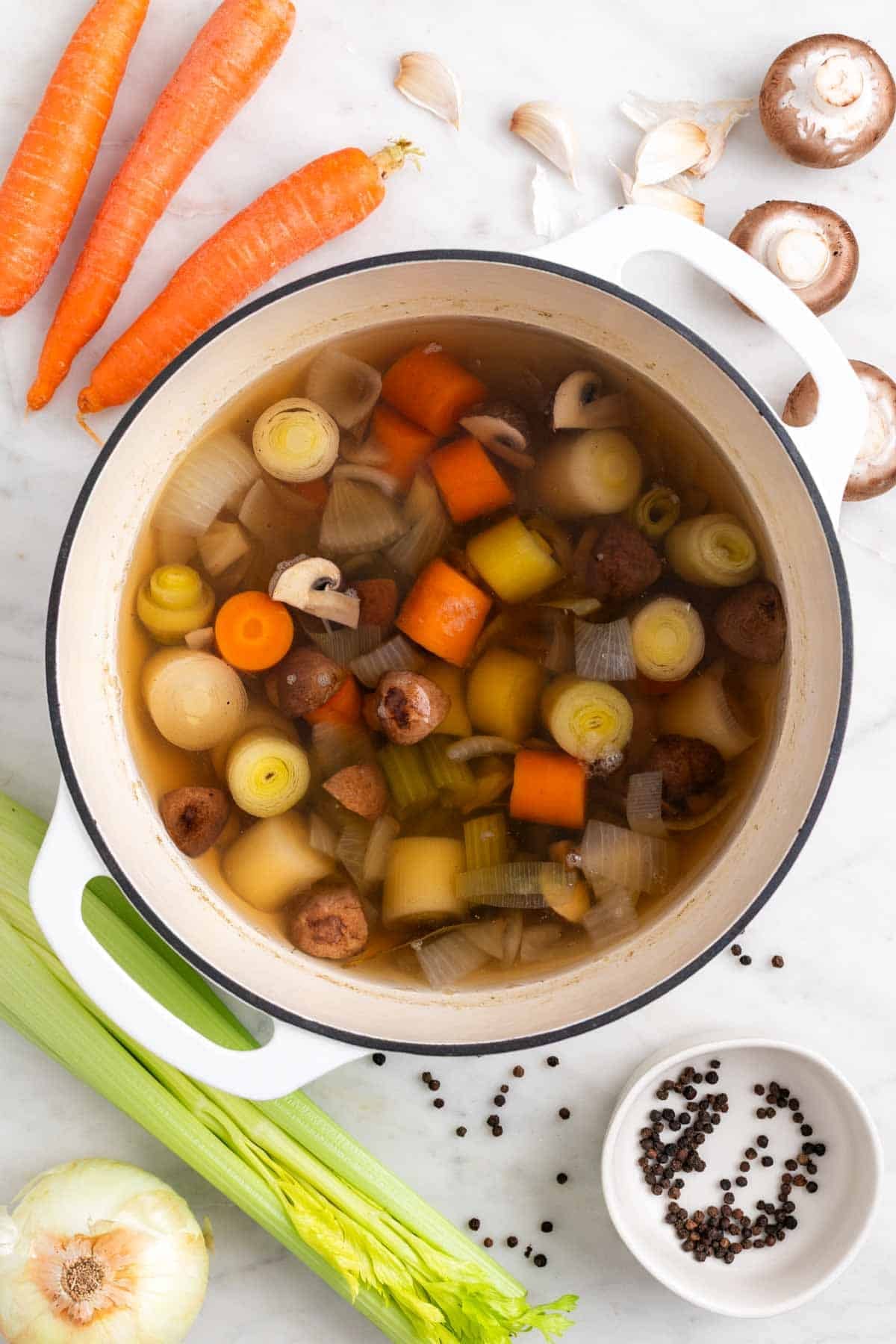 Pot with homemade vegetable broth and vegetables, with ingredients around it