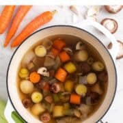 Large pot of homemade vegetable broth with vegetables and ingredients around it