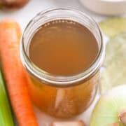 Homemade vegetable broth in a glass jar with vegetables around it