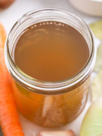 Homemade vegetable broth in a glass jar with vegetables around it