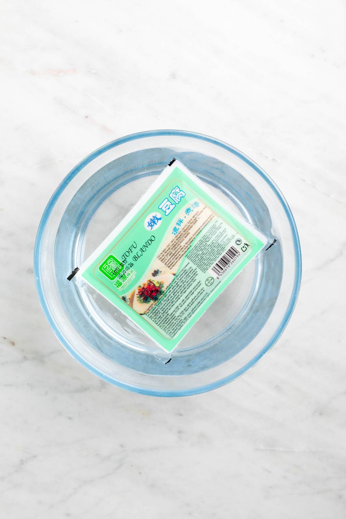 Block of frozen tofu thawing in a bowl of water