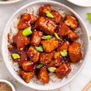 Bowl of crispy Korean BBQ tofu over rice with chopsticks and toppings around
