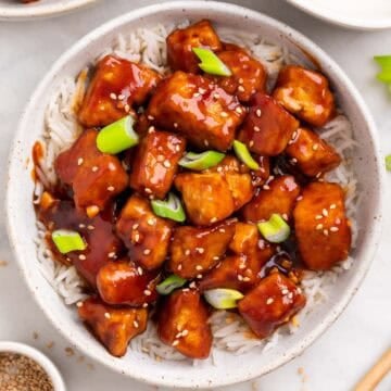 Bowl of crispy Korean BBQ tofu over rice with chopsticks and toppings around