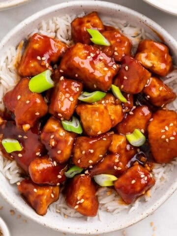 Bowl of crispy Korean BBQ tofu over rice with chopsticks and toppings around