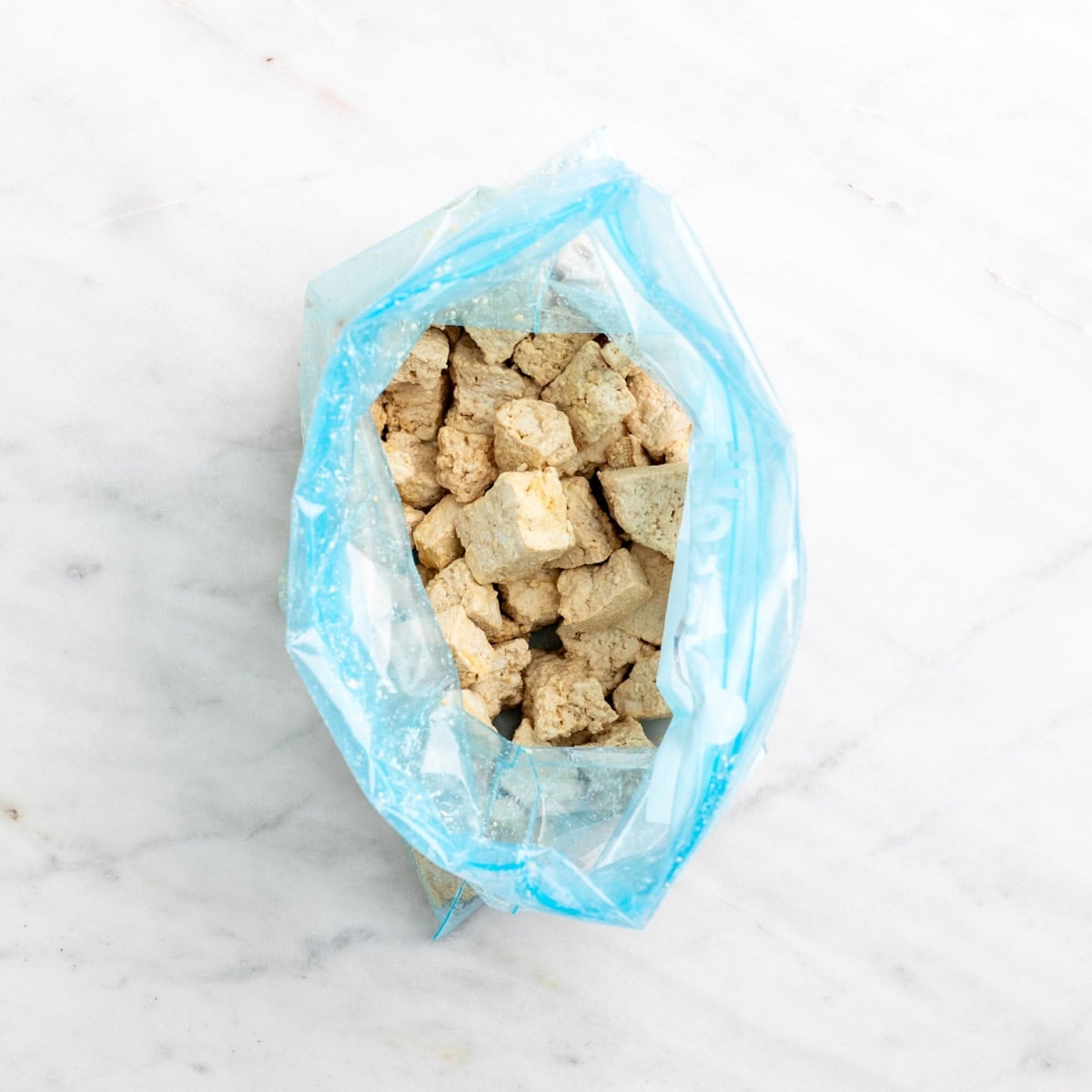 Torn tofu pieces coated with cornstarch in a freezer bag