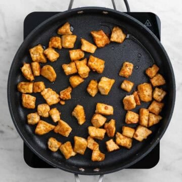 Crispy tofu pieces cooking in a skillet