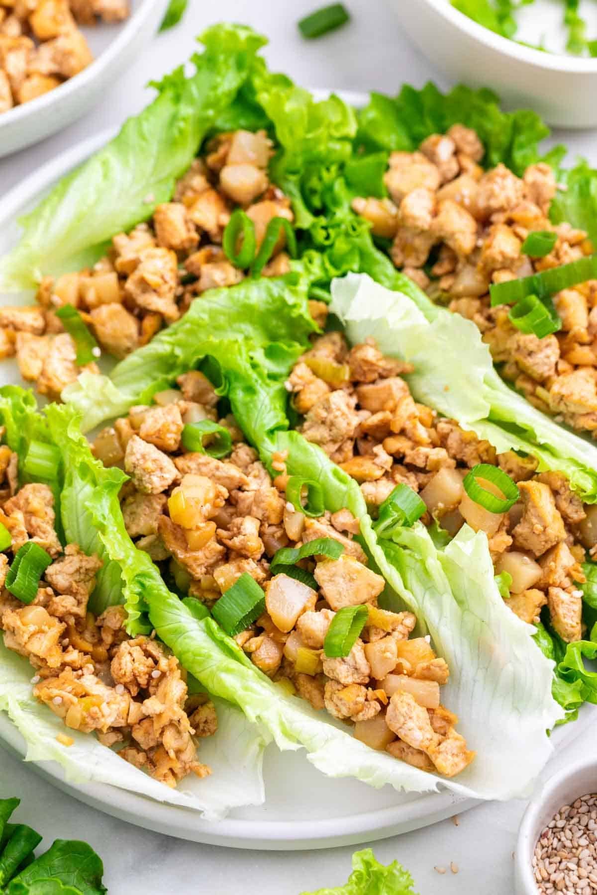 Tofu lettuce wraps served on a plate with sesame seeds and sliced green onions