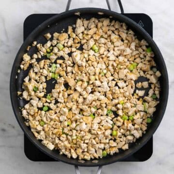 Crumbled tofu with garlic, ginger, and white parts of green onions cooking in a skillet