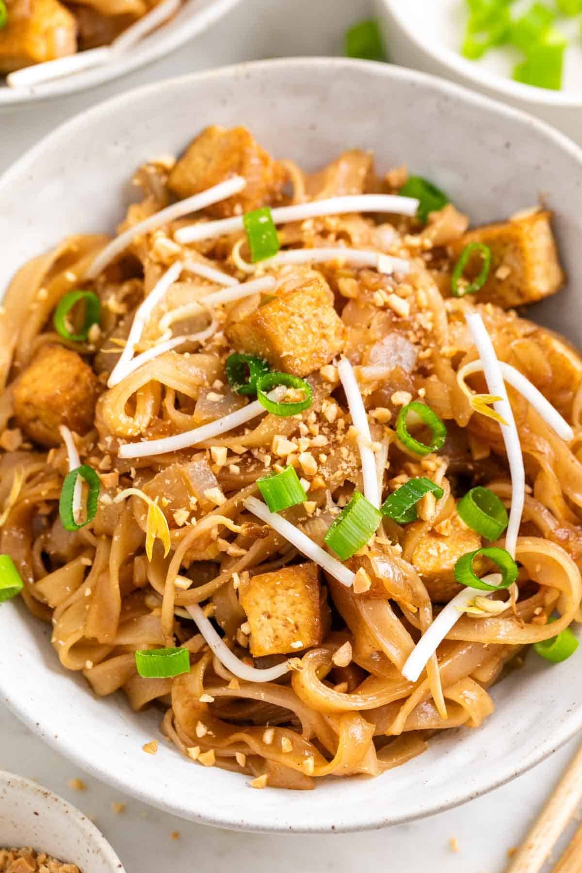 Homemade tofu pad Thai served in bowls with chopsticks and toppings on the side