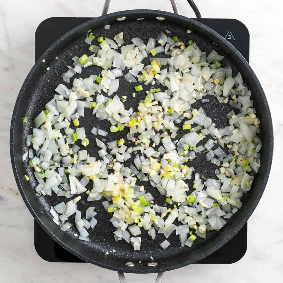 Garlic, onion, and green onions cooking in a skillet