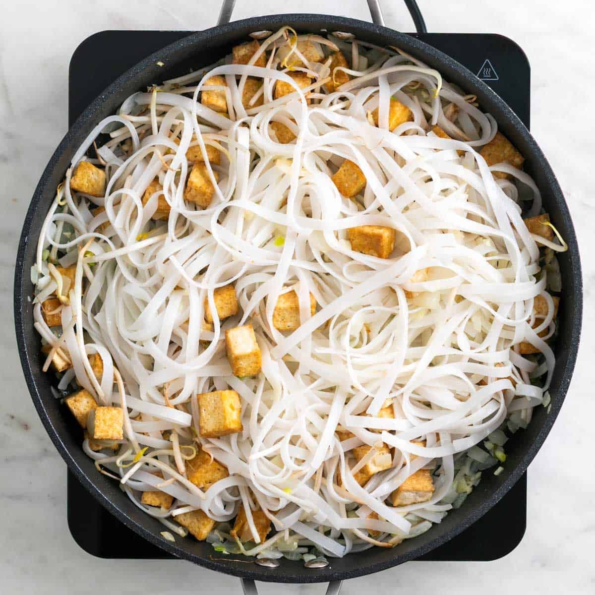 Tofu, vegetables, and rice noodles in a skillet