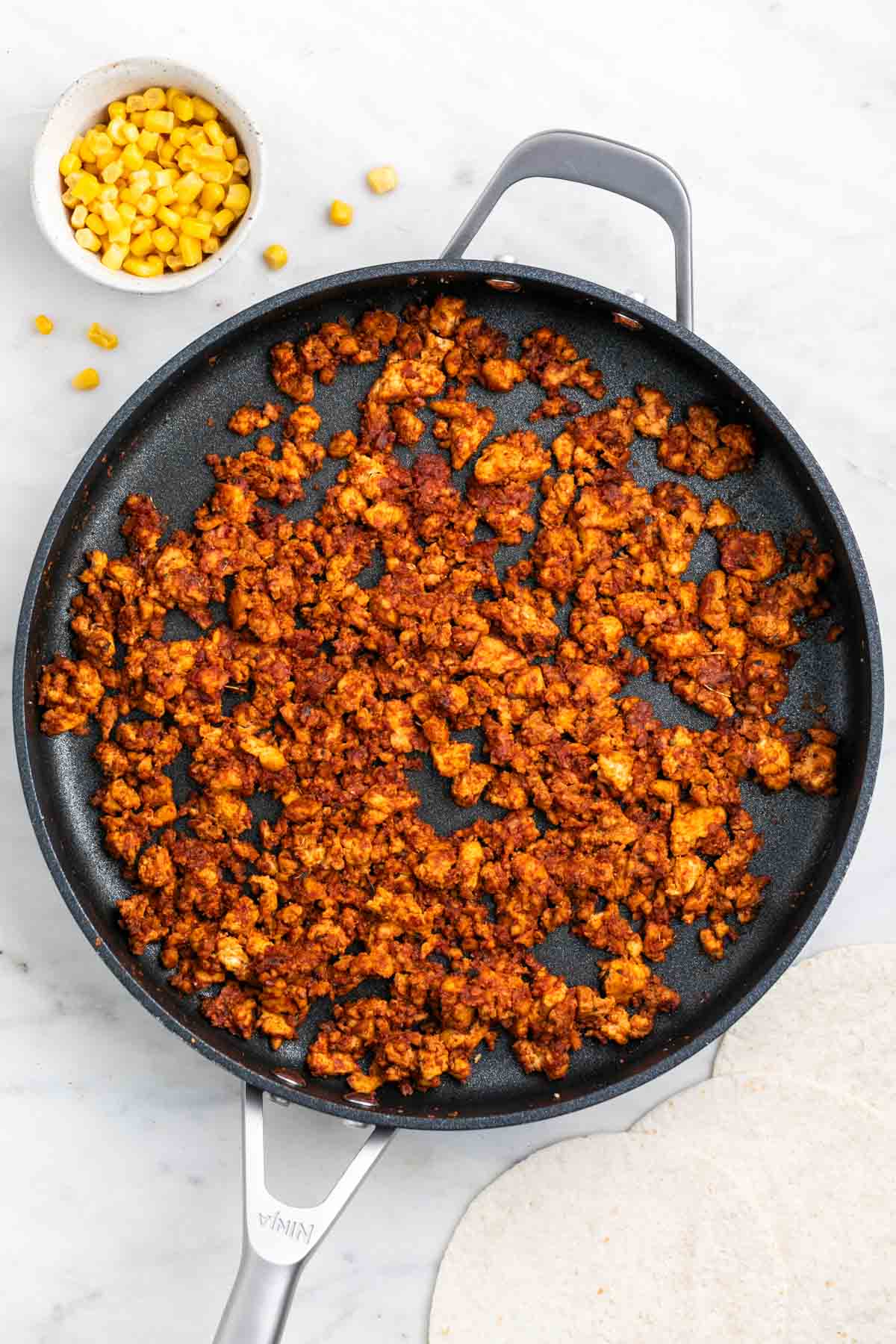 Skillet with tofu taco meat and corn with tortillas on the side