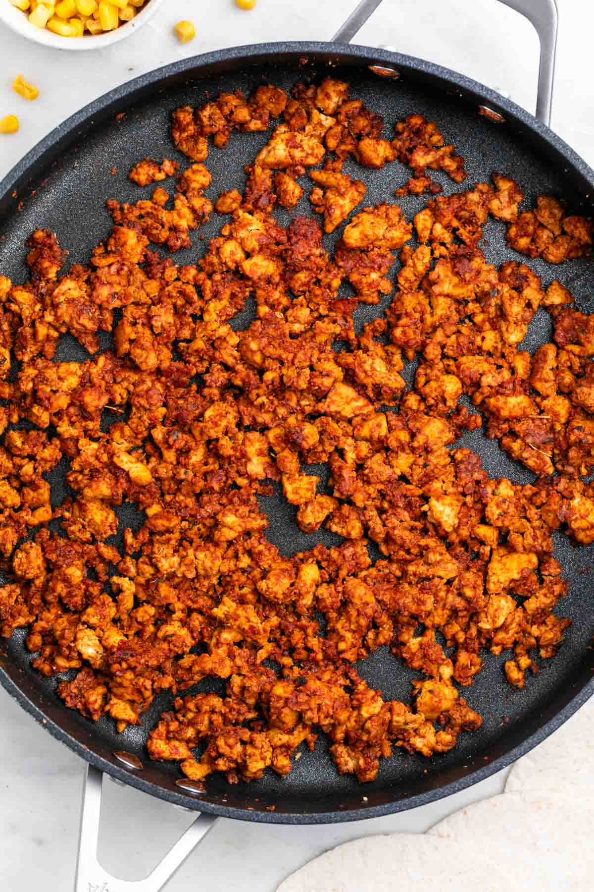 Tofu taco meat in a skillet with corn and tortillas nearby
