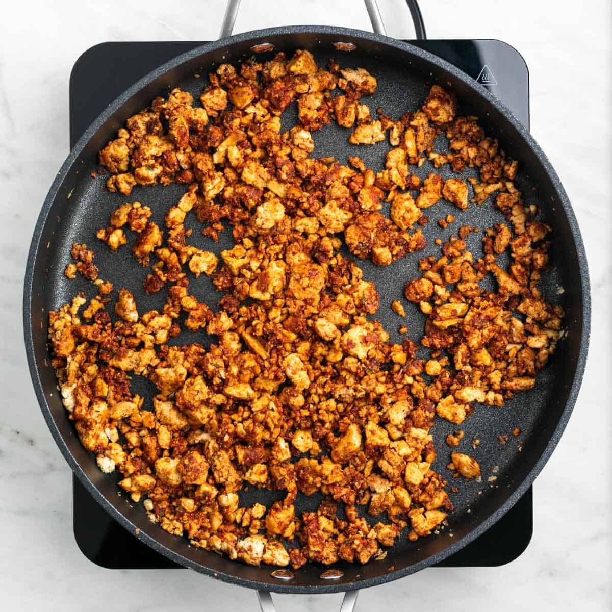 Crumbled tofu cooking with spices in a skillet