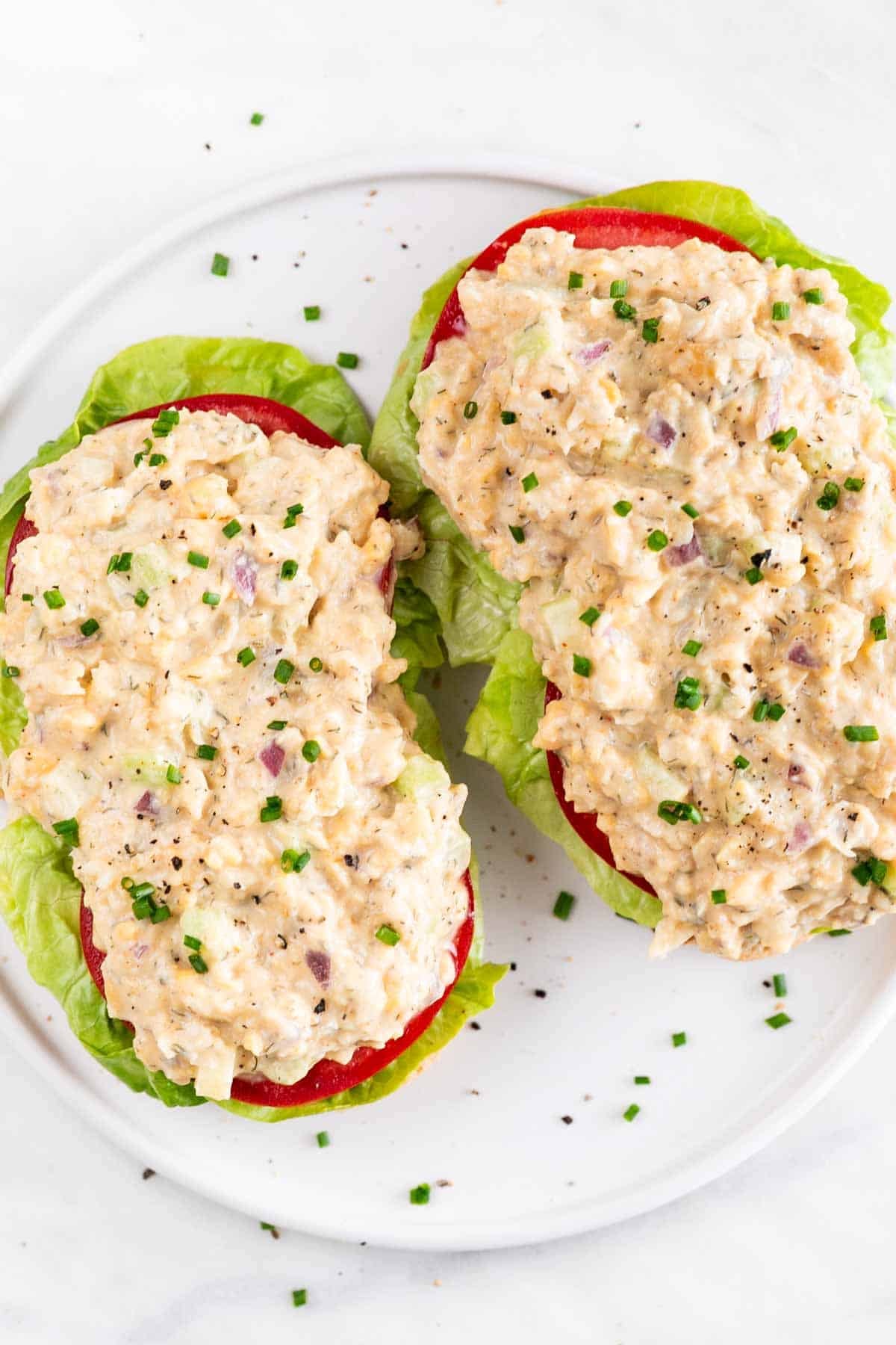 Vegan chicken salad toast with lettuce, tomato, chives, and black pepper on a white plate