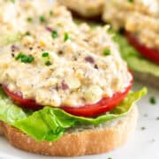 Two pieces of toast with vegan chicken salad, lettuce, tomato, chives, and black pepper