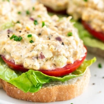 Two pieces of toast with vegan chicken salad, lettuce, tomato, chives, and black pepper
