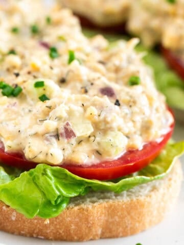 Two pieces of toast with vegan chicken salad, lettuce, tomato, chives, and black pepper