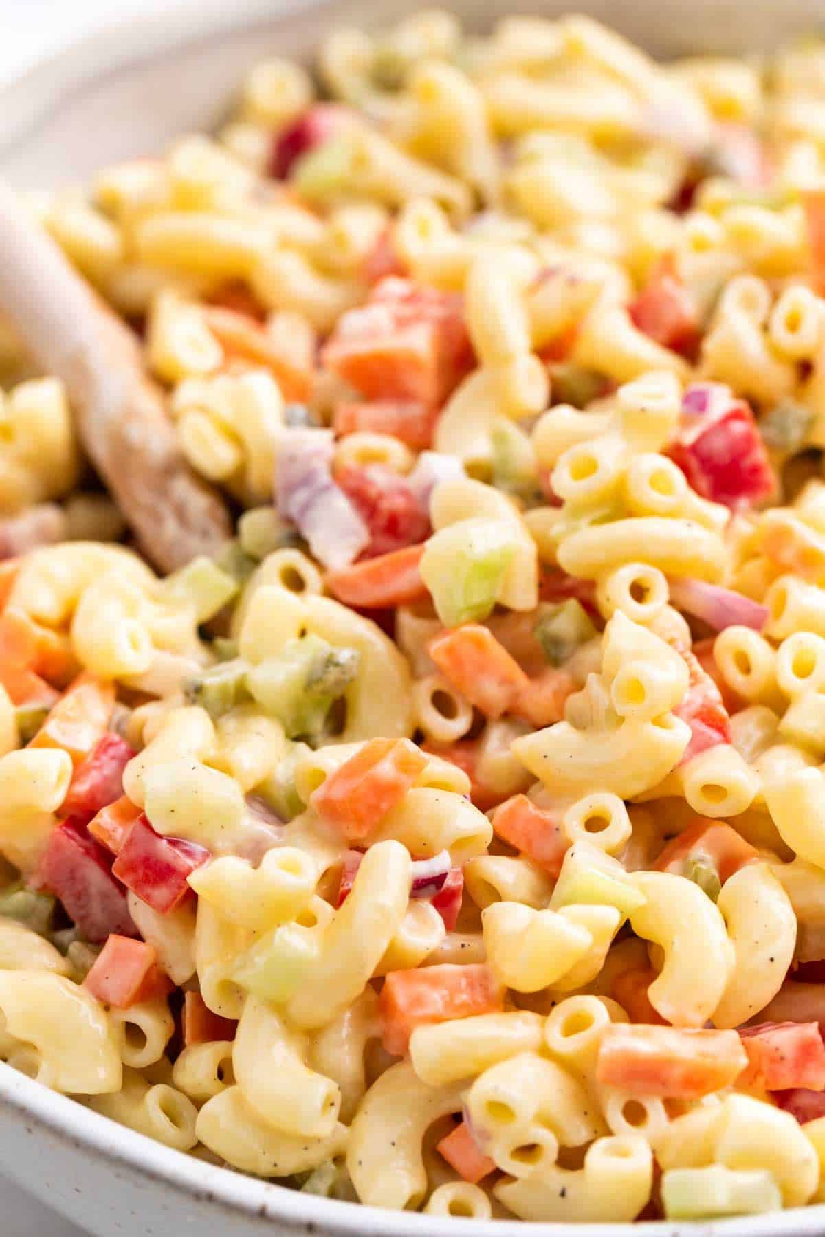 Large bowl of vegan macaroni salad with a wooden spoon