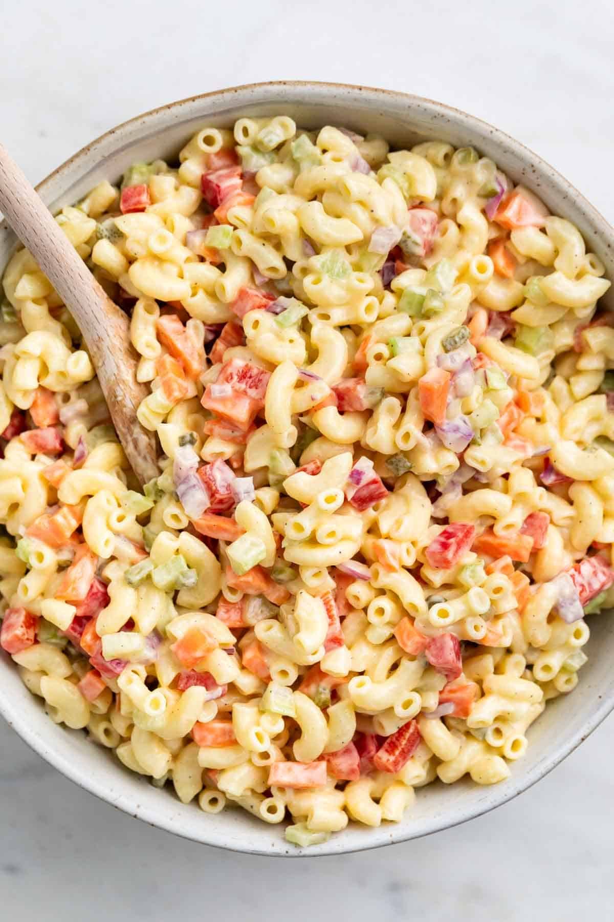 Creamy vegan macaroni salad in a large serving bowl with a wooden spoon
