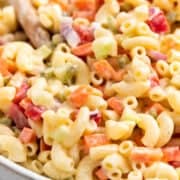 Vegan macaroni salad with crunchy vegetables in a large bowl with a wooden spoon