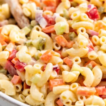 Vegan macaroni salad with crunchy vegetables in a large bowl with a wooden spoon